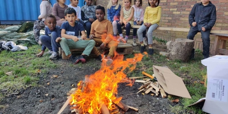 Børn sidder ved bål udenfor
